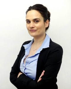 woman with dark hair tied up and arms crossed with blue shirt